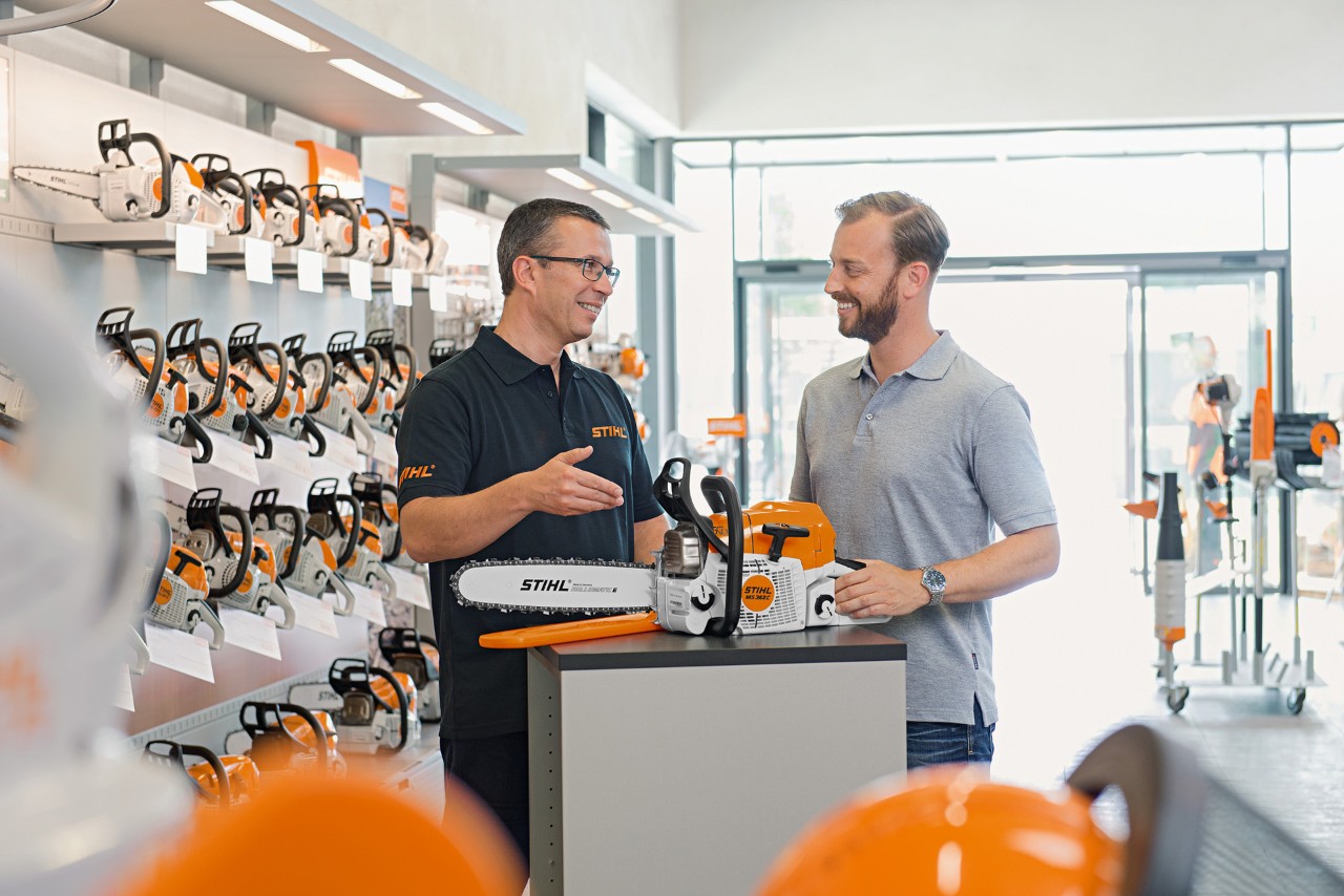 Sprzedawca STIHL doradza mężczyznom przy zakupie pilarki łańcuchowej STIHL