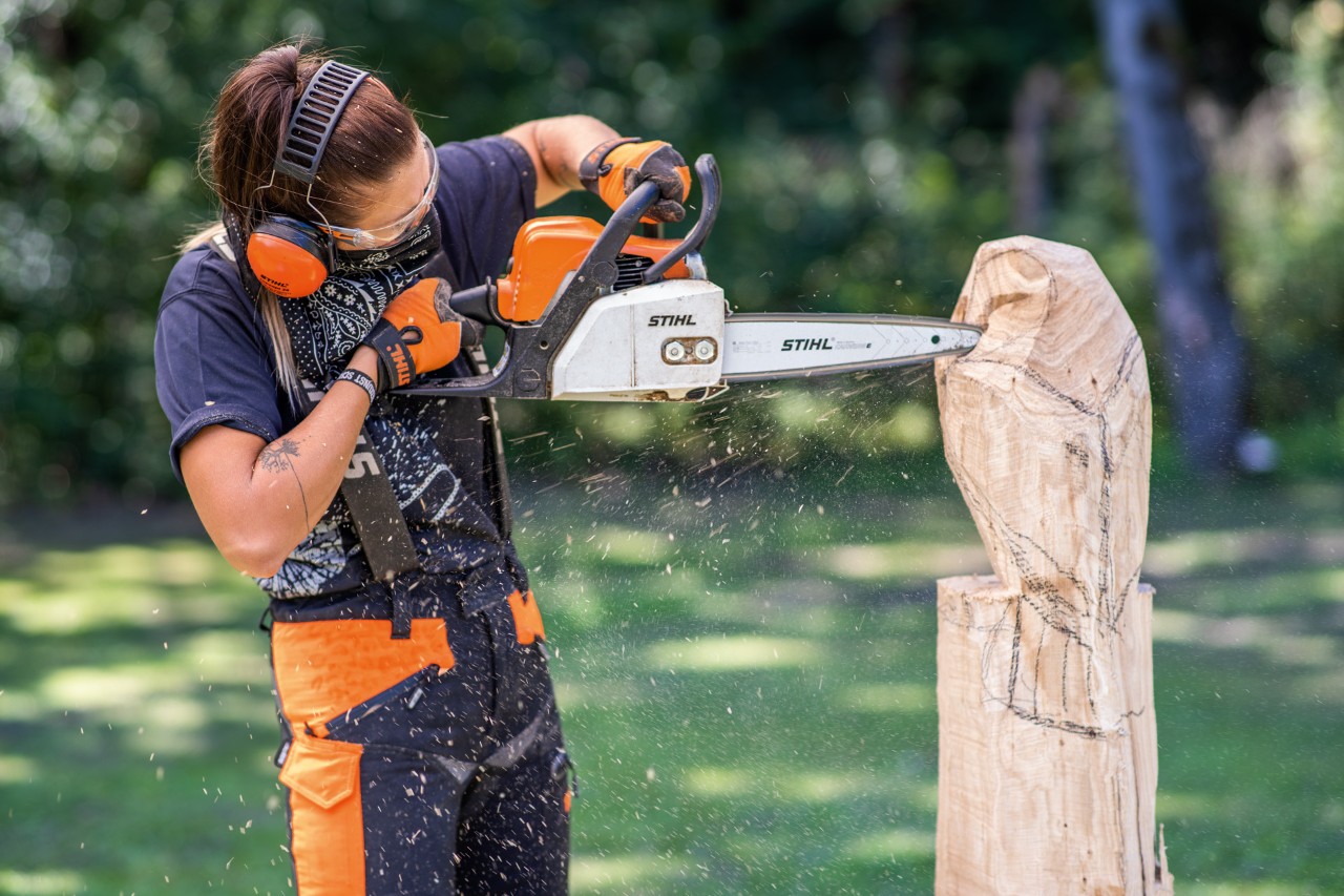 Kobieta w ochraniaczach słuchu STIHL rzeźbiąca drewnianą sowę za pomocą pilarki łańcuchowej