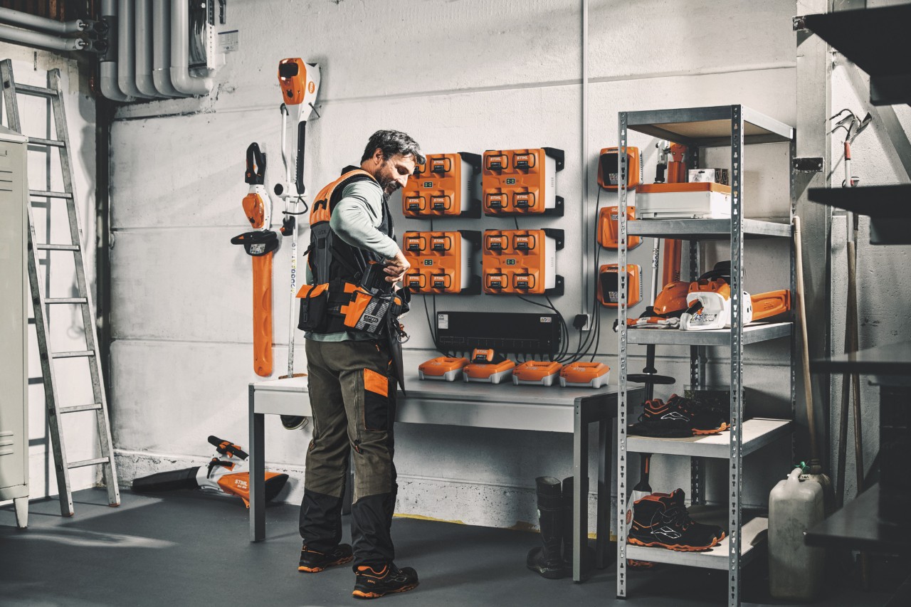 Mężczyzna w magazynie z urządzeniami i akumulatorami STIHL noszący modułowy system pasów STIHL ADVANCE X-Flex 