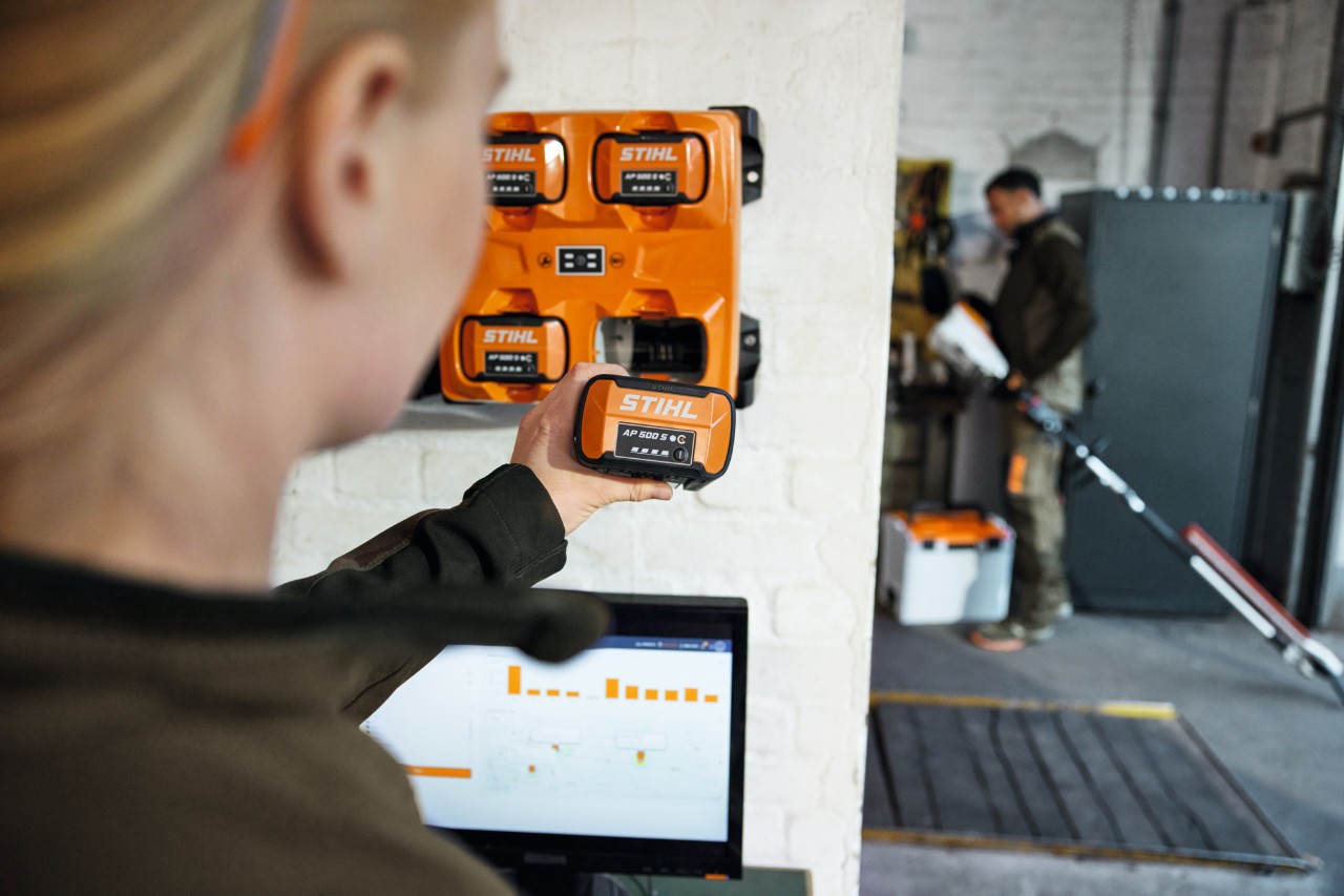 Kobieta przed laptopem wyjmuje AP 300 S z ładowarki wielofunkcyjnej STIHL AL 301-4