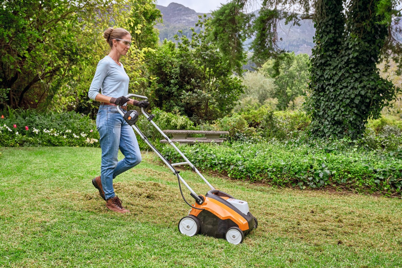 Kobieta w okularach i rękawicach ochronnych kosi łąkę kosiarką STIHL
